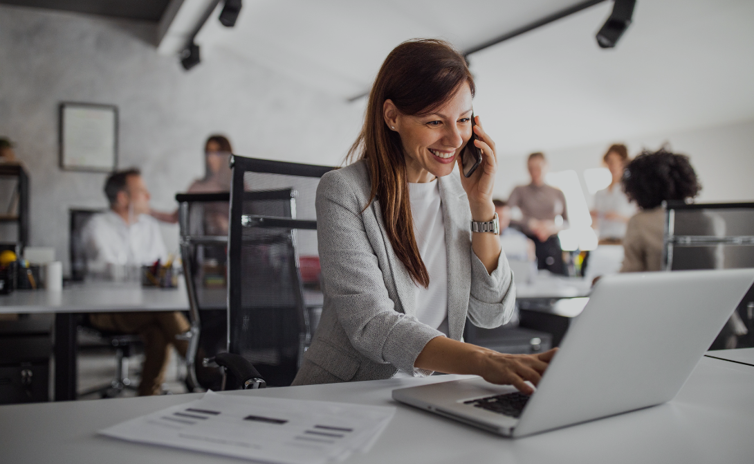 Smiling businesswoman talking on the phone while working on a laptop – representing successful omnichannel strategy and digital commerce alignment.