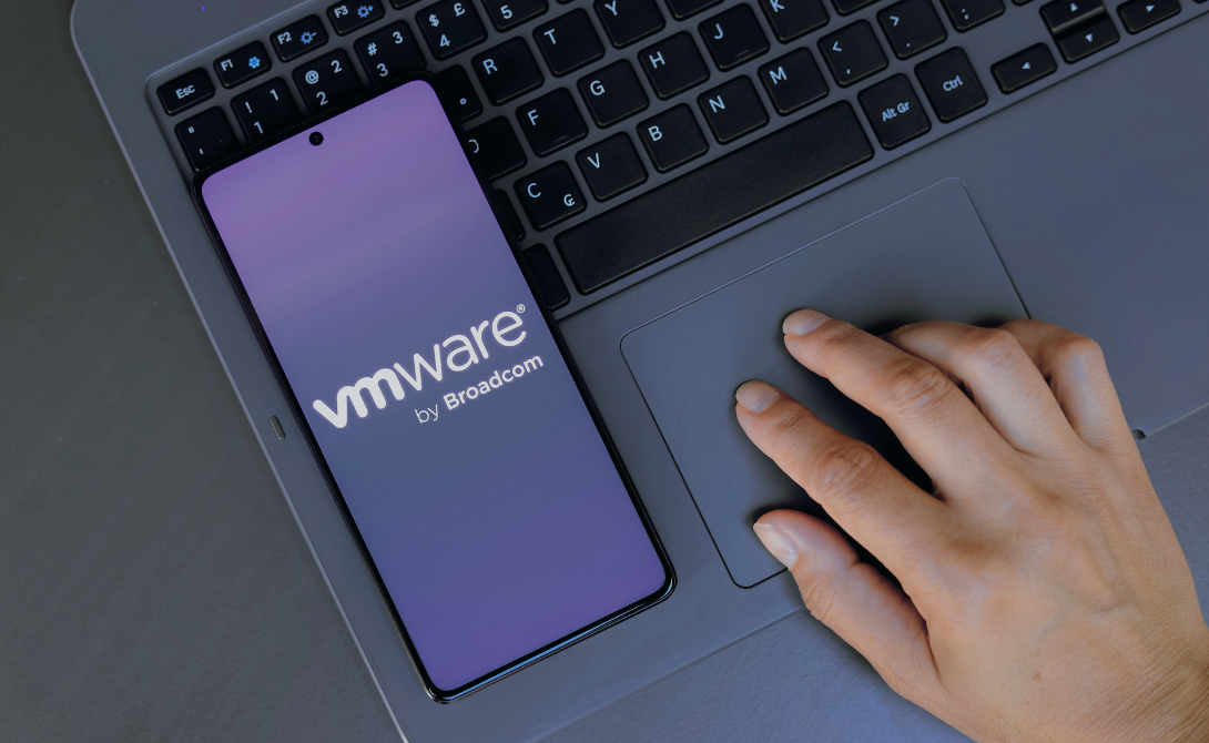 Smartphone displaying the VMware by Broadcom logo placed on a laptop – symbolizing Broadcom’s acquisition of VMware and its strategic impact on businesses.