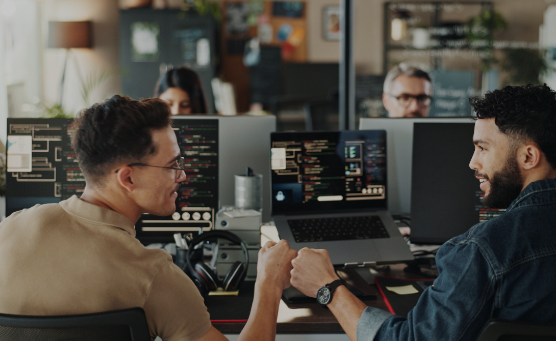 Two developers fist bumping in front of low-code app interfaces on screen.